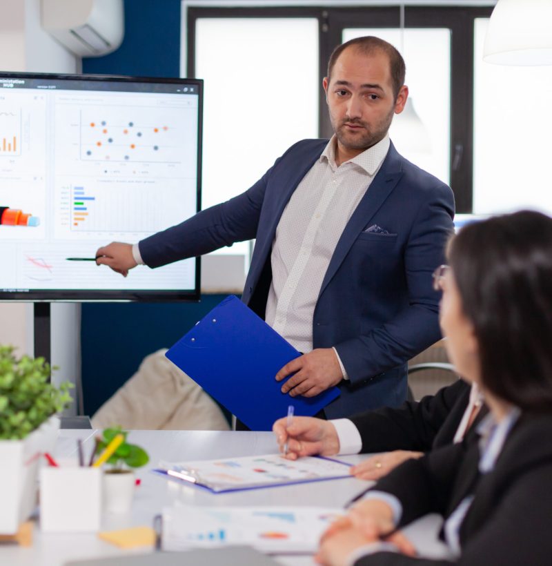 Successful team leader briefing pointing explaining project in conference room brainstorming. Corporate staff discussing new business application with colleagues looking at screen